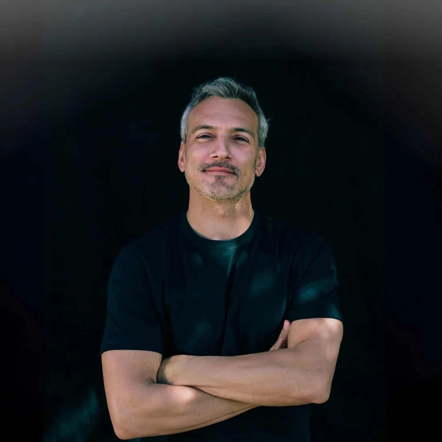 Mann steht entspannt mit verschränkten Armen vor dunklem Hintergrund für natürliche Männerhautpflege