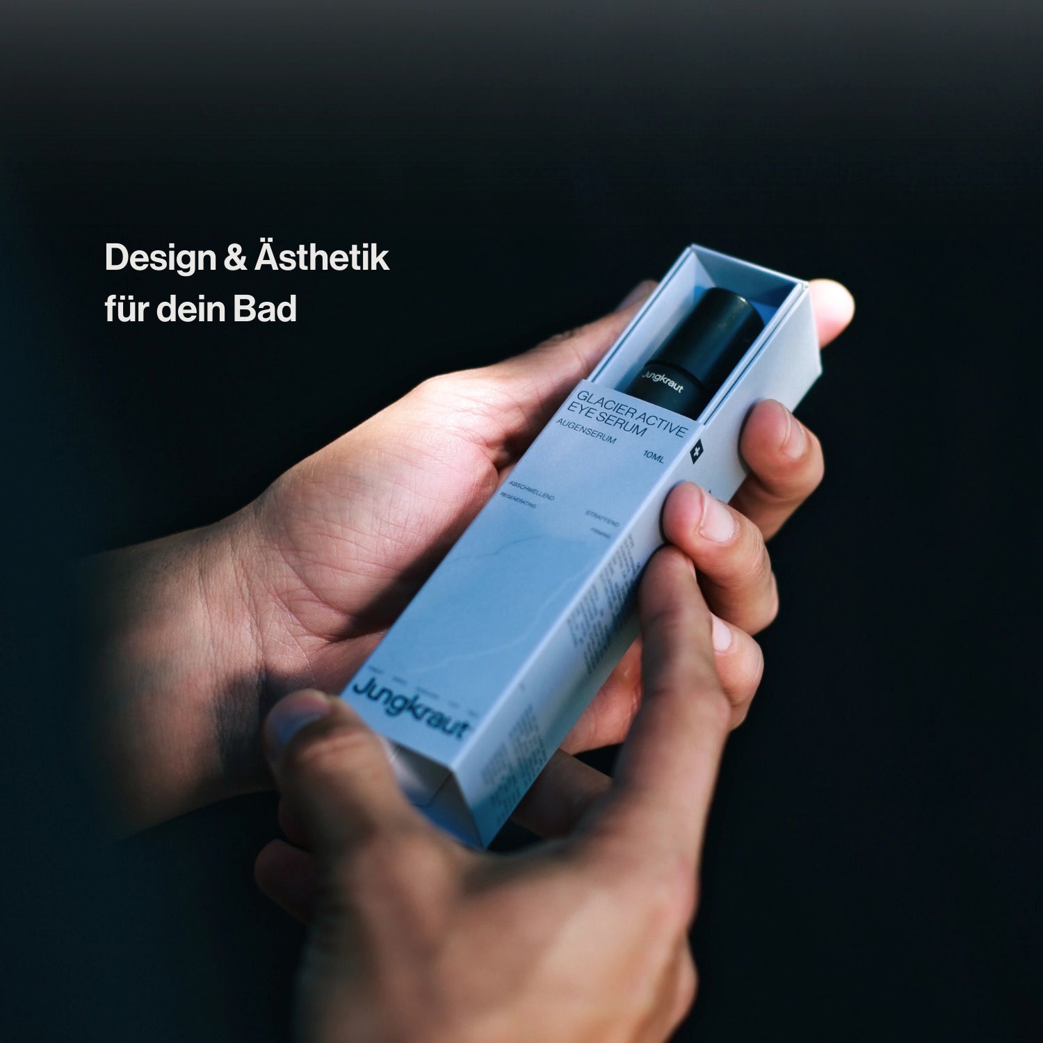 Nahaufnahme von Händen, die das Jungkraut Glacier Active Eye Serum aus der eleganten weißen Verpackung nehmen. Links im Bild steht der Text „Design & Ästhetik für dein Bad“. Das Bild betont die hochwertige Verarbeitung, das moderne Verpackungsdesign und den Anspruch an stilvolle Männerroutine.